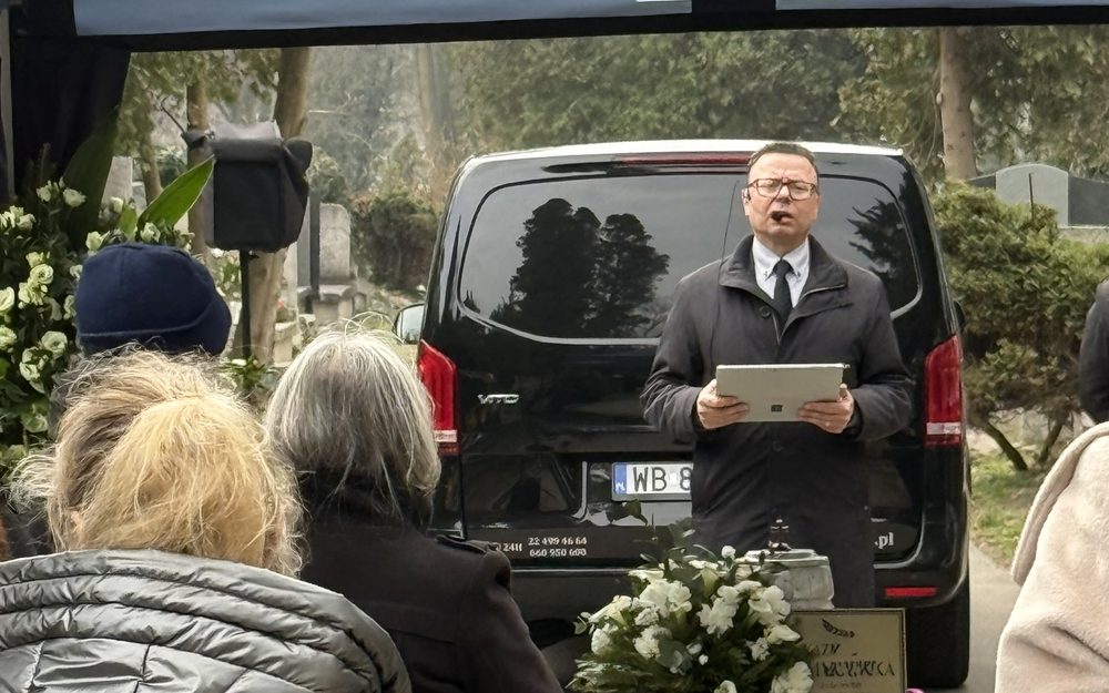 Uczestnicy pożegnania na cmentarzu, w ciemnych płaszczach
